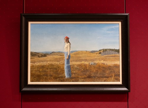 A painting of a woman standing in a field of dried grass, with hills and blue skies behind her.