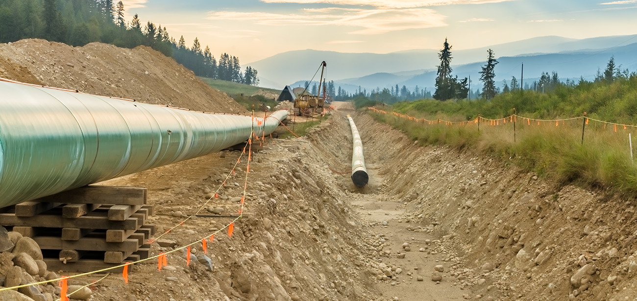 Pipeline construction work in progress with trees and a mountain range in the background. 