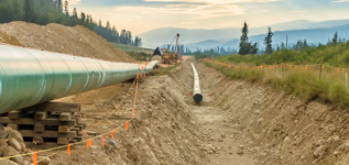 Pipeline construction work in progress with trees and a mountain range in the background. 