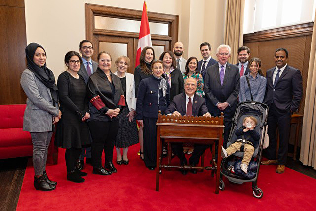 Des amis et des membres de la famille du sénateur Al Zaibak, dont l’ancien premier ministre Joe Clark, debout à sa gauche, assistent à la cérémonie d’assermentation de ce dernier, le 6 février 2024. Également présents sur la photo, de gauche à droite : Nafisah Chowdhury, Ruba El-Sayegh, Karl Tabbakh, Roula El-Rifai, Evva Massey, Jana Al Zaibak, Mona Al Zaibak, Najla Al Zaibak, Rami Alhamad, Leen Al Zaibak, Michael Henry, Eugene Henry, Charlotte Chummar, Noble Chummar et Dean Henry. (Crédit photo : Bureau du sénateur Mohammad Al Zaibak)