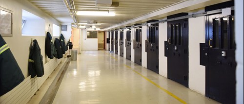 An indoor hallway of a prison block with individual cells on the right side.