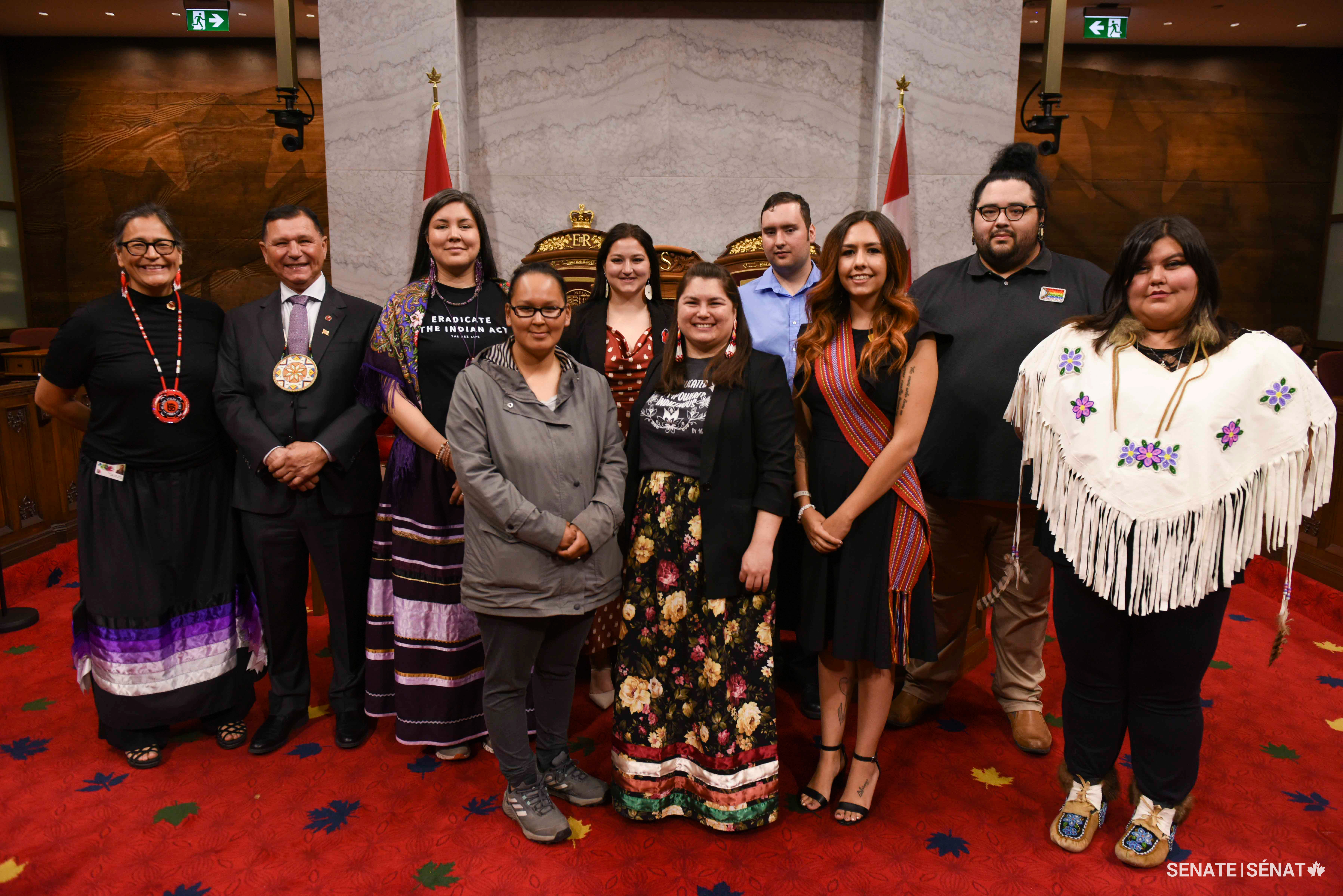 Senators and participants of Voices of Youth Indigenous Leaders 2023 pose in the Red Chamber.   Back row, from left: Senators Michèle Audette and Brian Francis, Audrey-Lise Rock-Hervieux, Chante Speidel, Dylan Adam and Bertram Bernard. Front row, from left: Dina Koonoo, Paula MacDonald, Katherine Merrell-Anderson and Helaina Moses.