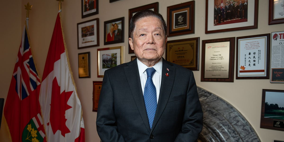 Le sénateur Victor Oh debout dans son bureau devant un mur de photos, d’articles et de certificats encadrés.