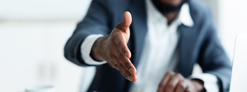 A Black man dressed in a suit extending his hand.