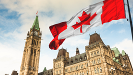 A Canada flag flying on a pole with Centre Block and the Peace Tower in the background.