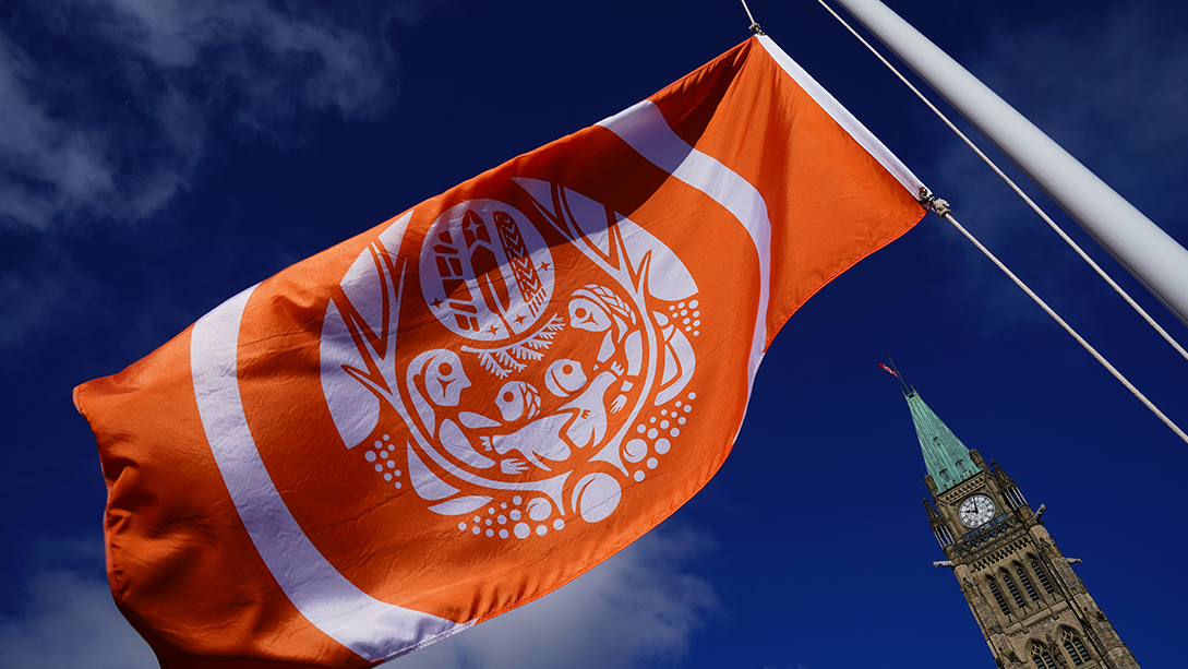 An orange flag flies with the Peace Tower in the background.